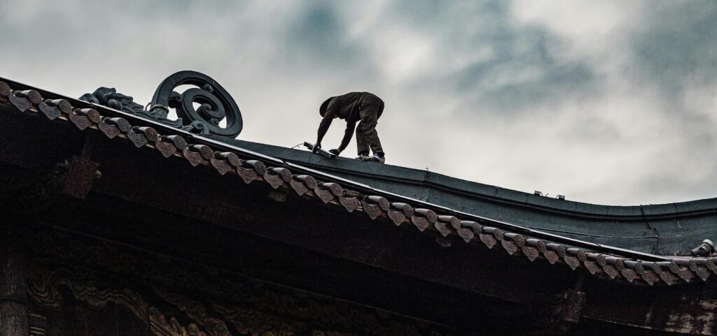 Worker inspecting and repairing a roof, highlighting the importance of timely roof maintenance and replacement.