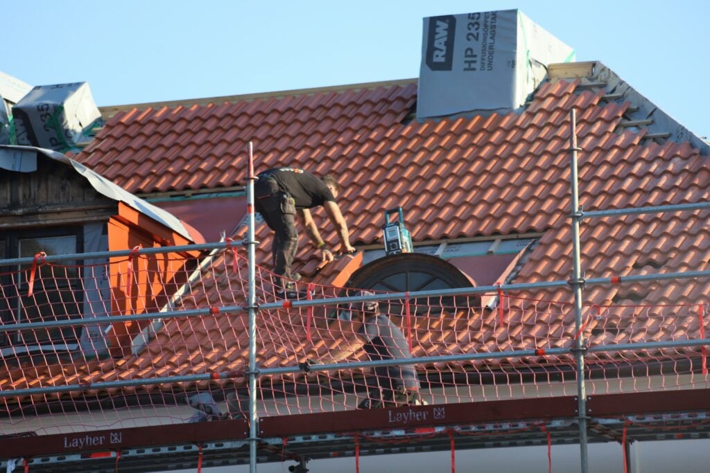 Roofer installing clay tiles on a residential roof, illustrating how homeowners can choose durable and weather-resistant roofing materials. Roofer installing clay tiles on a residential roof, illustrating how homeowners can choose durable and weather-resistant roofing materials.