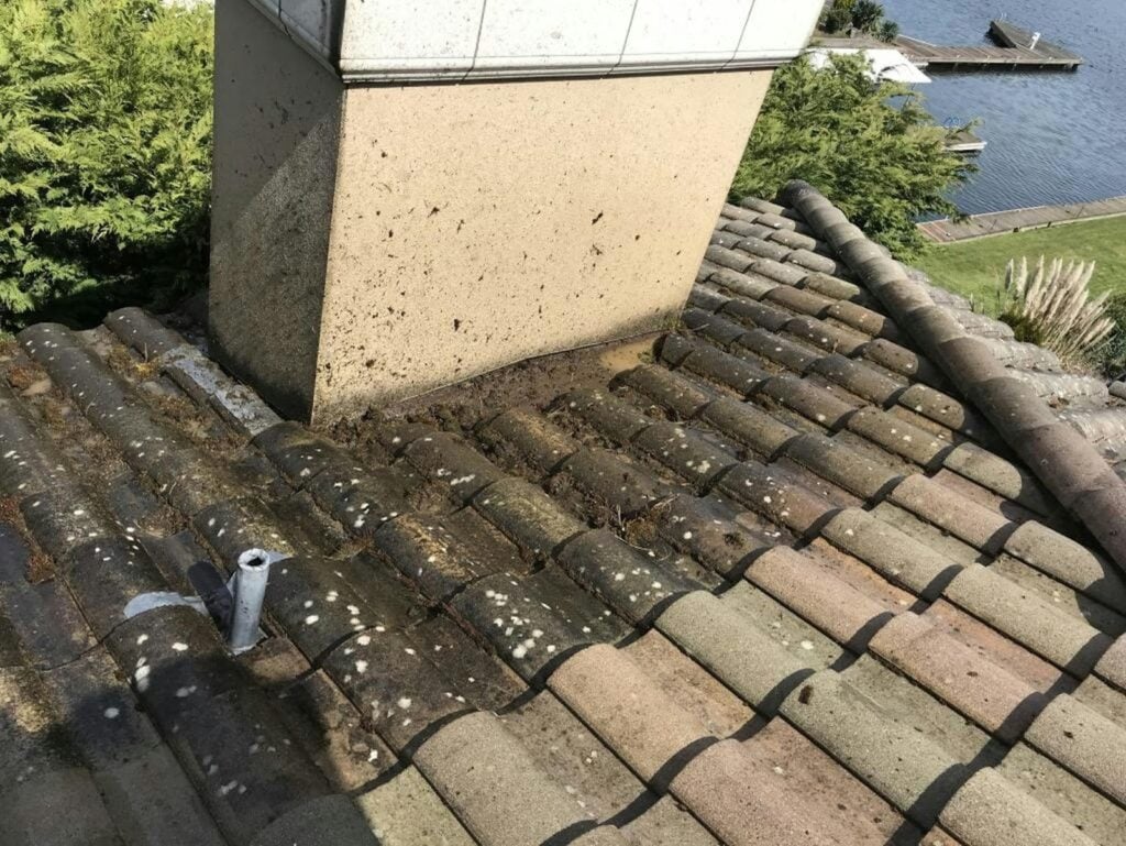 Aging roof tiles and debris buildup around a chimney, illustrating common conditions that can lead to roof leaks in Tampa Bay homes.
