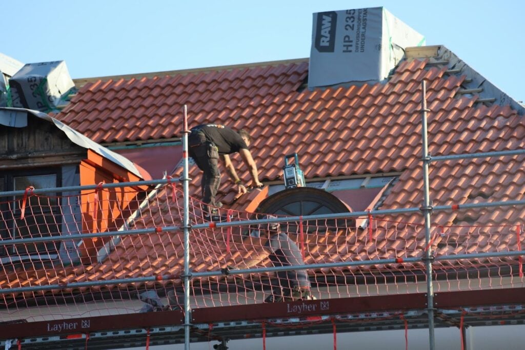 Roofing contractor installing clay roof tiles on a residential property, illustrating key roofing services such as roof installation, repair, and replacement offered by GenX Roofing in Tampa.