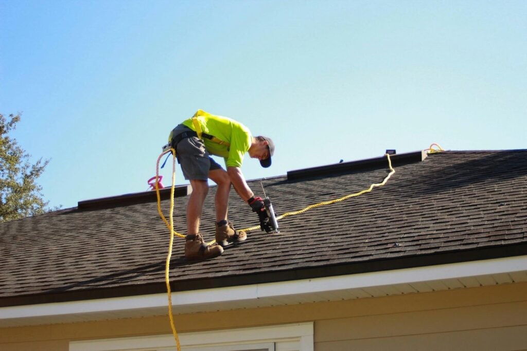 Roofer installing shingles on a residential roof, demonstrating proper installation and maintenance practices that help extend the lifespan of a roofing system.