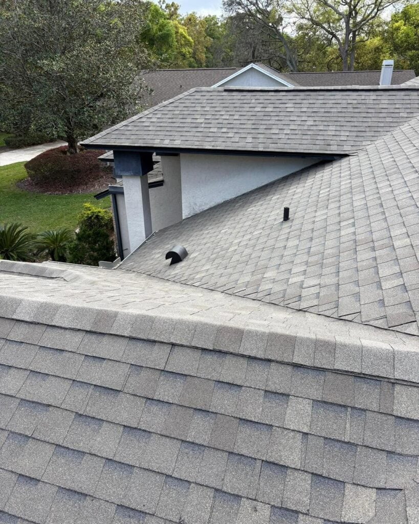 Aerial view of a residential roof with gray shingles surrounded by trees and neighboring homes